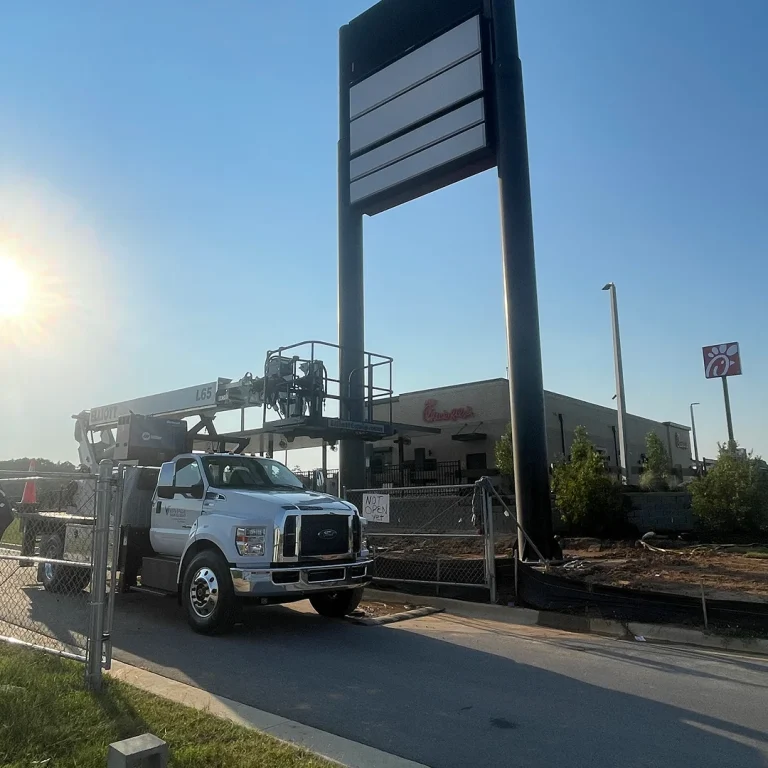 Large blank pylon sign structure with Vintage Sign & Light bucket truck on-site at a new Chick-fil-A location.