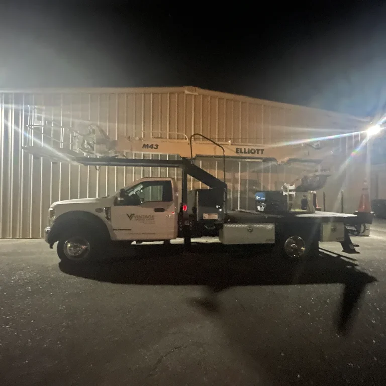 Vintage Sign & Light service truck with Elliott lift parked at night outside a commercial facility.