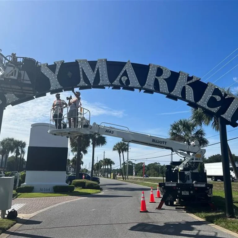 Technicians servicing illuminated channel letters on large archway entrance at a shopping district.