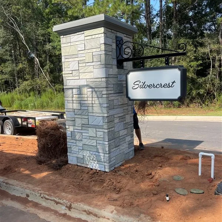 Custom hanging sign for Silvercrest mounted on a stone pillar monument during final installation phase.