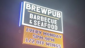 Illuminated Brewpub sign with a barbecue and seafood cabinet above a digital message display.