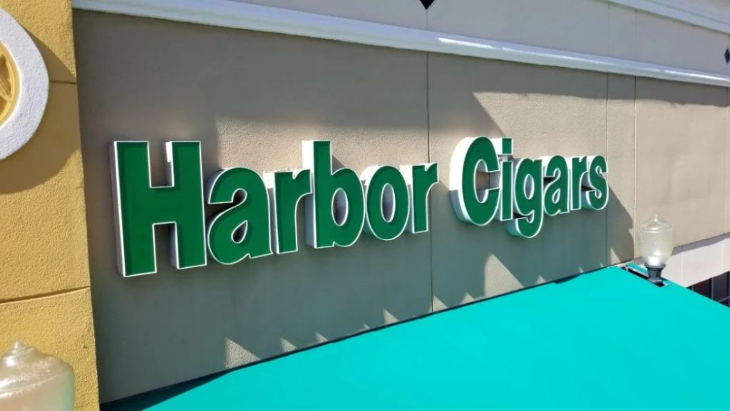 Green “Harbor Cigars” channel letter sign mounted on a storefront facade above a turquoise awning.