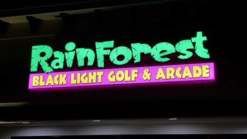 Illuminated Rainforest Black Light Golf & Arcade storefront sign with green and pink lighting.