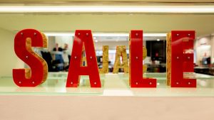 s a Prominent "SALE" sign made of individual, red, three-dimensional letters with visible fasteners or lights, set up in a store window display