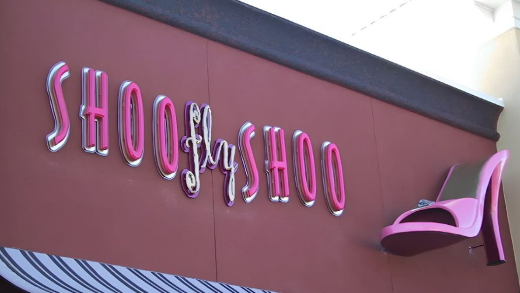 Pink “Shoo Fly Shoo” storefront lettering with a large high-heel graphic mounted on the building facade.