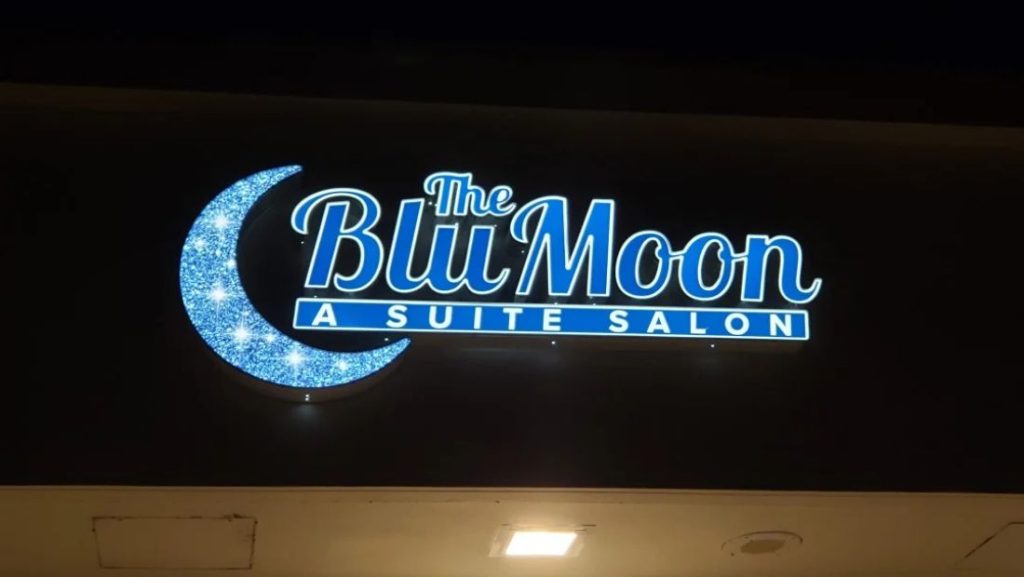 Illuminated The Blu Moon A Suite Salon sign with a glowing crescent moon and blue lettering at night.