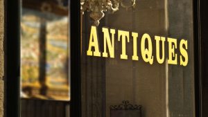 Gold "ANTIQUES" sign displayed on a glass storefront window, representing elegant and timeless Retail Store Display Signs for boutique shops.