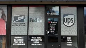 Storefront window graphics for Ship Pensacola showing USPS, FedEx, UPS, and shipping service information.