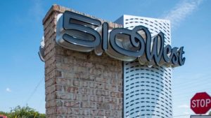 Brick monument sign featuring large, modern 3D lettering that reads “510 West” with a decorative fish pattern background.