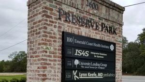 Brick monument sign displaying business listings for Emerald Coast Health Institute, IS4S, University Lending Group, and Lynn Keefe, MD Pediatrics.