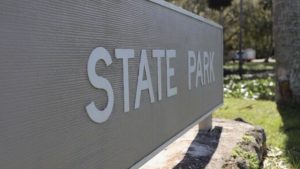 Close-up view of metal monument signs featuring raised white letters spelling 'State Park' on a textured gray background in an outdoor park setting.