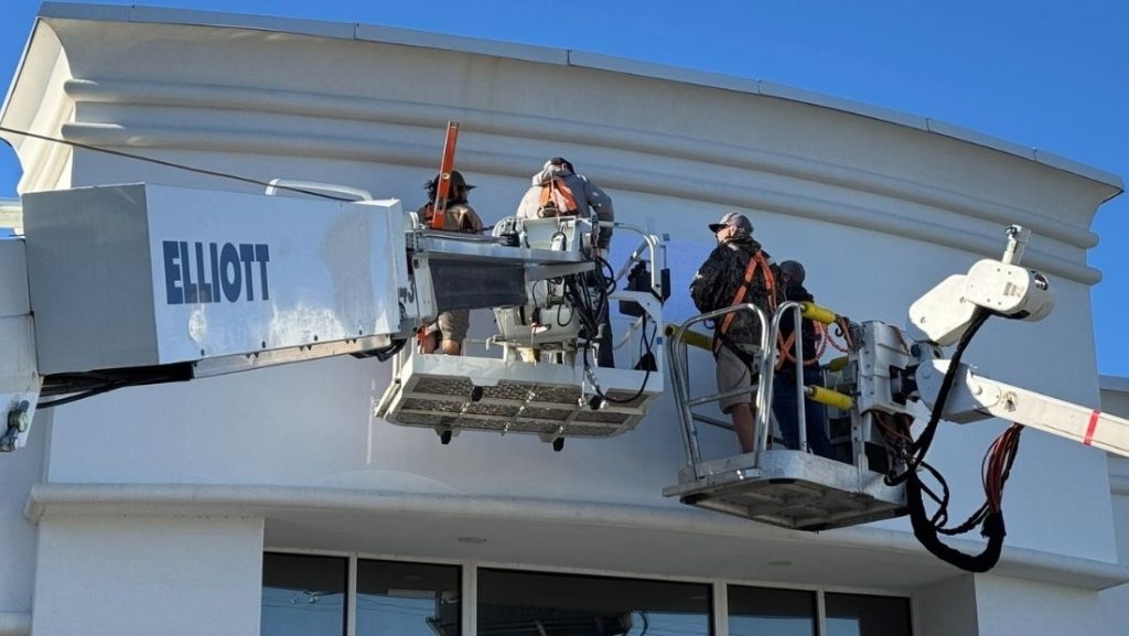 Workers using a boom lift to install signage on a building, demonstrating professional sign design and engineering.