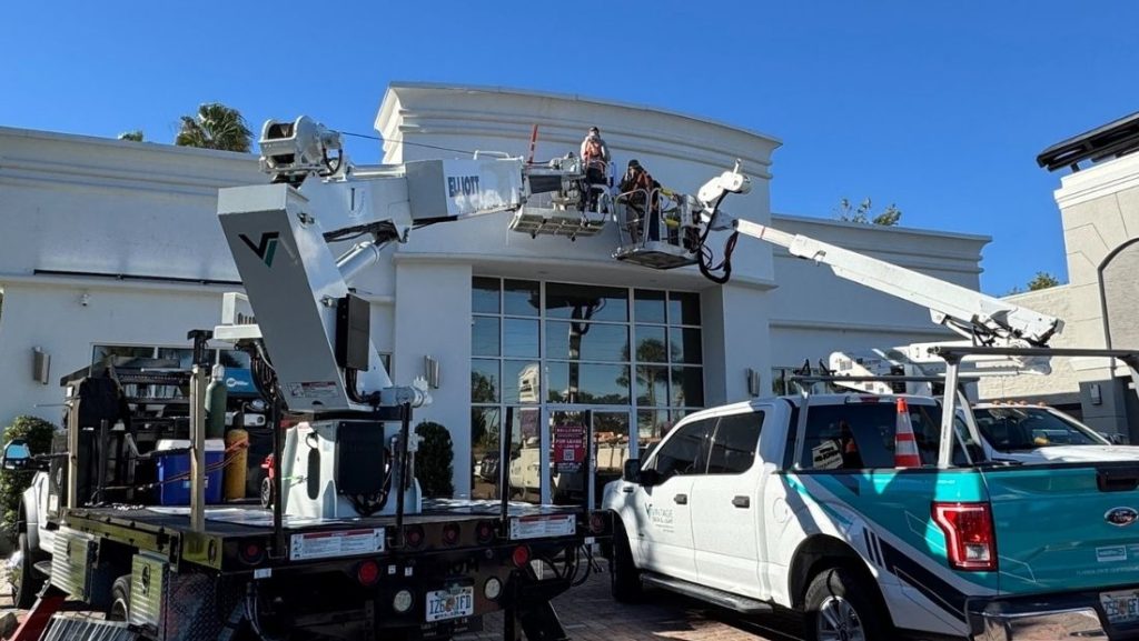 Workers using lift trucks to install a storefront sign on a commercial building, showing equipment and crew in action as part of a cost comparison local vs national installation services for storefront signs.