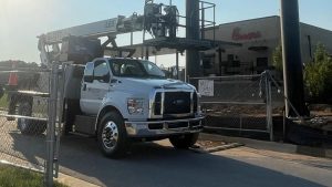 A truck with a mounted lift used for installing signage at a construction site, with a sign indicating 'Not Open Yet' in the background. Sign installation services in action.
