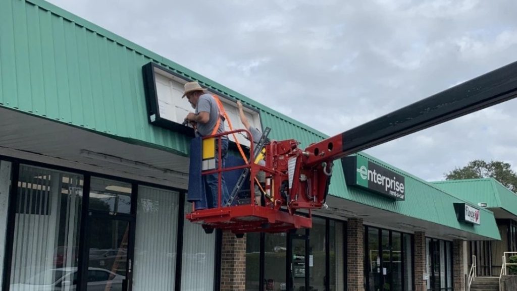 A worker using a lift to install a sign above a storefront, showcasing sign installation services for a business.