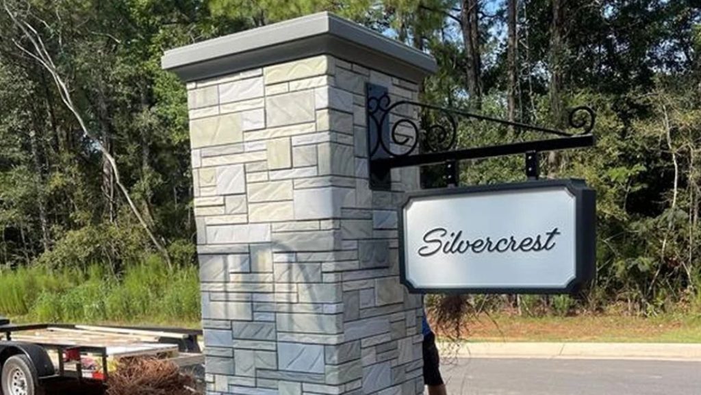 Stone monument sign with a hanging panel that reads “Silvercrest,” installed outdoors along a wooded roadside.
