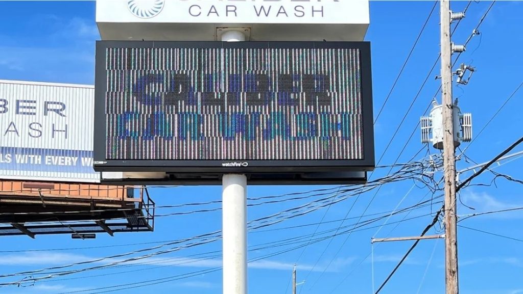 Digital signage providers display a promotional message for Caliber Car Wash on a vibrant electronic screen, showcasing modern signage solutions for businesses.