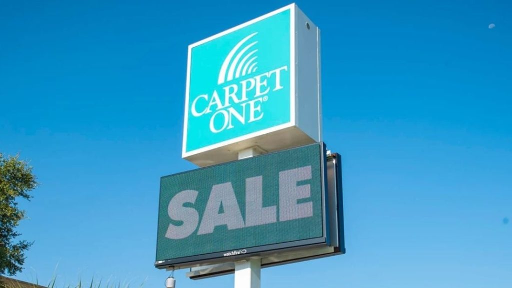 Digital signage providers display a 'SALE' message on an electronic sign outside a Carpet One store, highlighting modern promotional signage solutions.