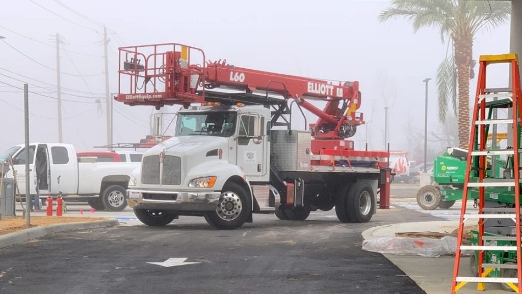 Digital signage exterior installation using a bucket truck and lift equipment on a commercial site, with technicians preparing outdoor signage infrastructure.