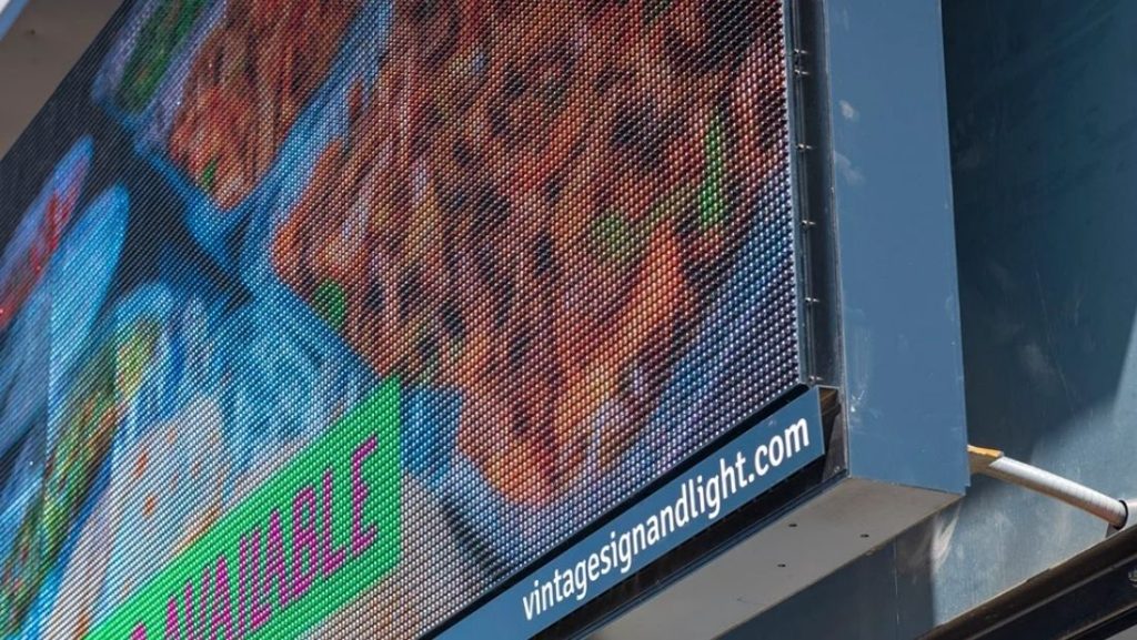 Close-up of in-store digital signage displaying vibrant food images and a promotional message, with the brand's website visible at the bottom.