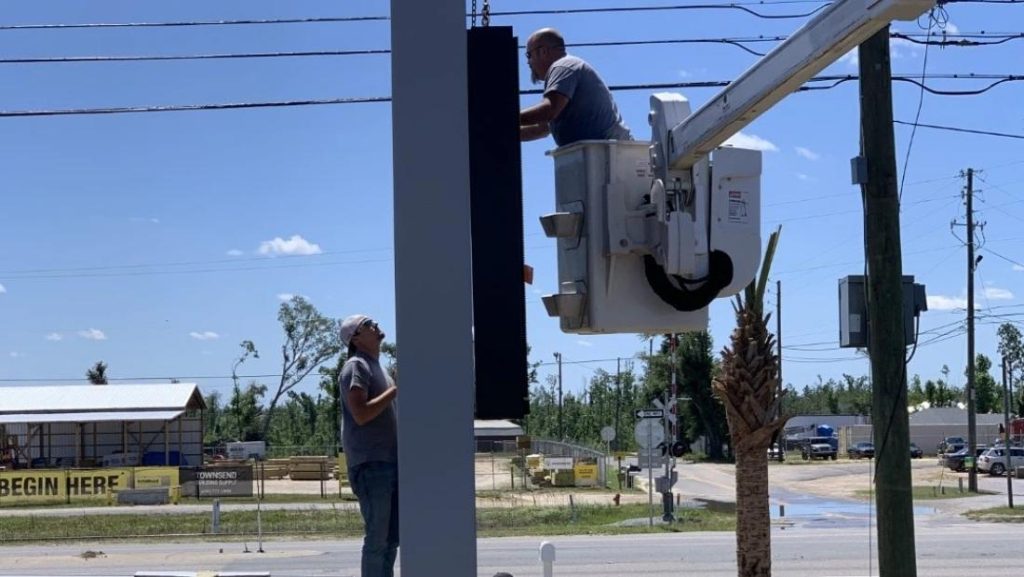Workers installing outdoor digital signage with a bucket truck in a sunny location.