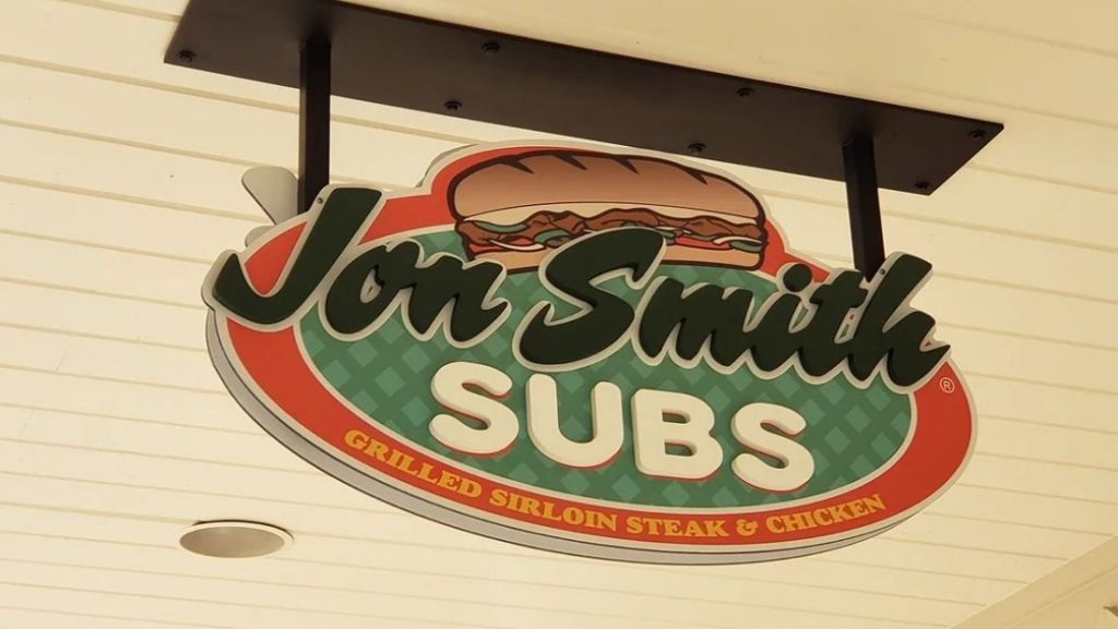 Hanging restaurant storefront sign for Jon Smith Subs professionally mounted under a covered exterior, showcasing clean and secure sign installation for business visibility.