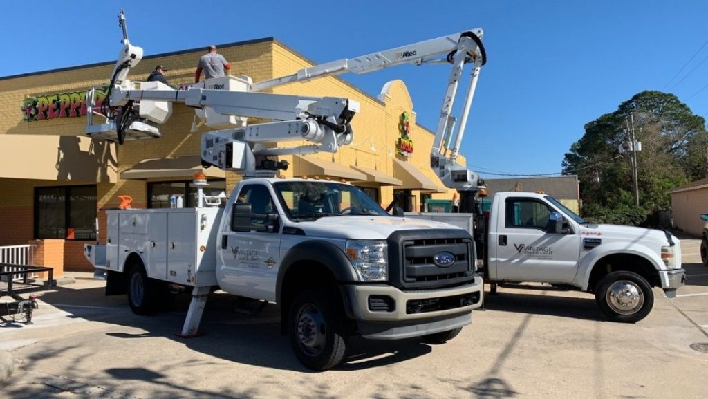 A professional sign installation crew using a bucket truck to install a large sign on a commercial building, showcasing the importance of proper equipment and expertise for different types of signs.