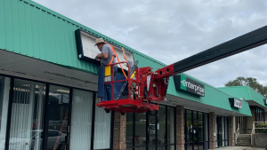 Installer working from an aerial lift on an exterior storefront sign.