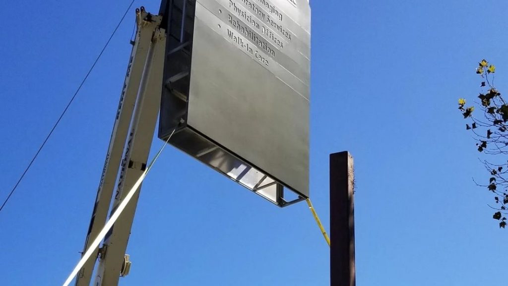 Crane lifting a large sign panel into place on a tall pole, installing a high-elevation pylon sign for maximum visibility.