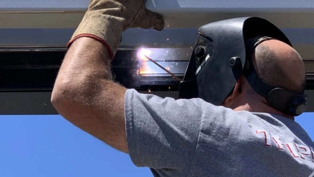Technician welding metal brackets with professional sign installation tools during commercial sign mounting on an exterior building facade.