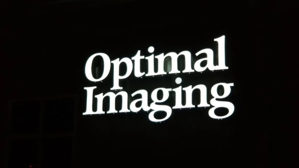 Illuminated “Optimal Imaging” storefront sign with bright white channel letters on a dark background, mounted for high visibility at night.