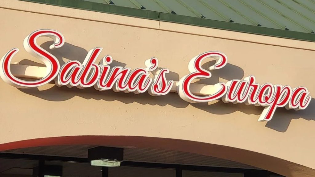 Storefront sign for Sabina’s Europa featuring red and white illuminated script channel letters mounted on a beige facade, illustrating how to install channel letters for retail signage.