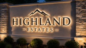 Halo-lit small monument sign reading 'HIGHLAND ESTATES' at night, showcasing the soft glow of the letters on a stone and stucco base