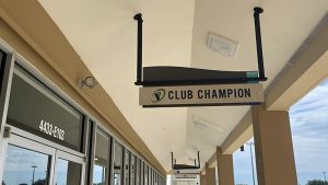 Club Champion hanging sign mounted above a covered storefront walkway.