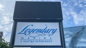 Outdoor digital signage display above the Legendary Marina monument sign against a blue sky.