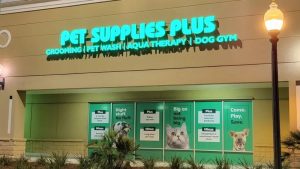 Illuminated Pet Supplies Plus channel letter sign with window graphics on a storefront at night.