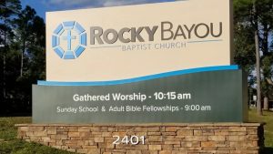 Rocky Bayou Baptist Church monument sign with worship times and stone base near the roadside.