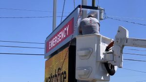 Technician using a bucket truck to install an emergency sign on a roadside digital display.