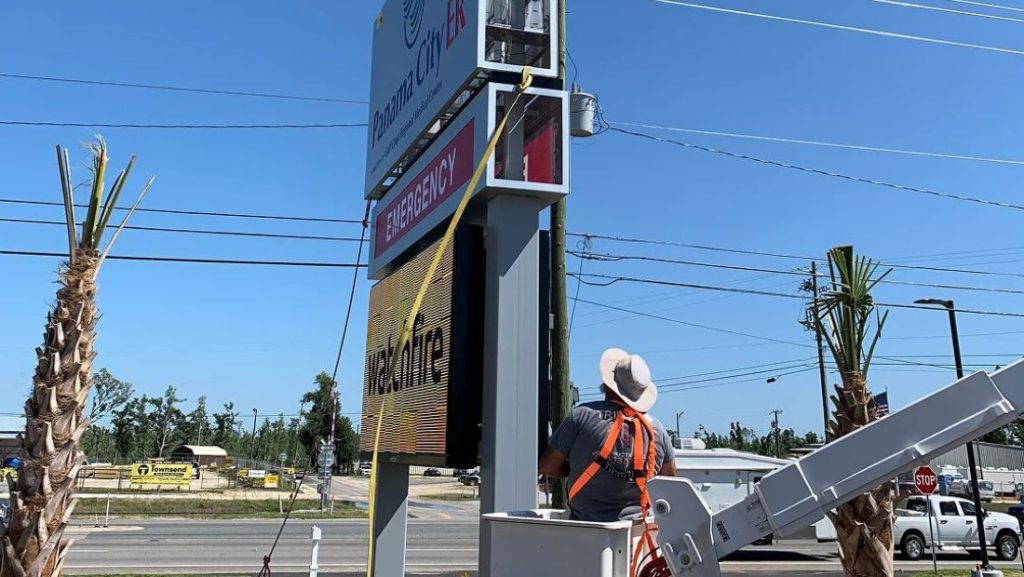 Vintage Sign & Light installer working from a lift beside a roadside digital sign.