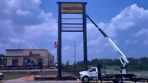 Tall Watchfire roadside sign structure with a service truck and lift positioned beside it.